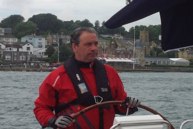 Antonio at the wheel of a boat looking out into the sea with a town in the background