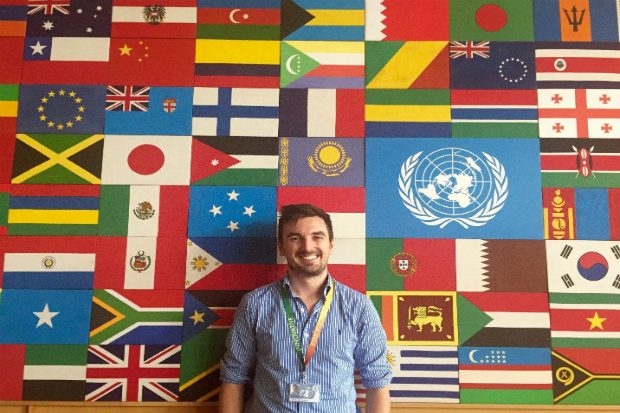 Daniel standing in front of a large number of flags from different countries