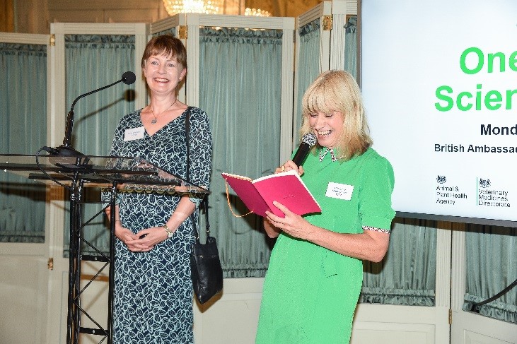 Christine standing on a stage holding a micrphone next to Kath Webster