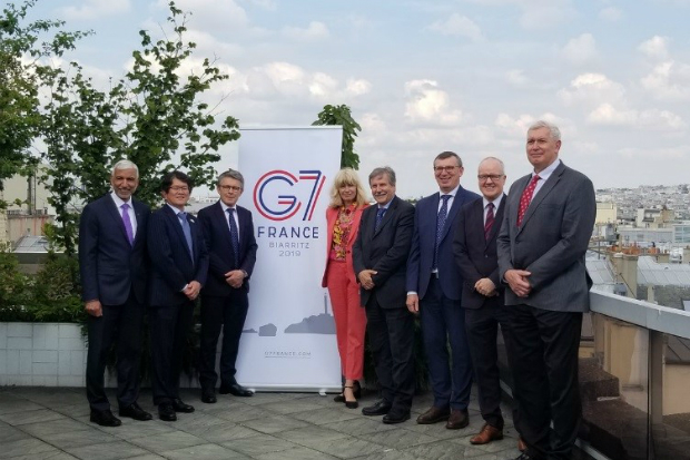 Eight people standing in front of a poster with G7 and a view of Paris in the background. 