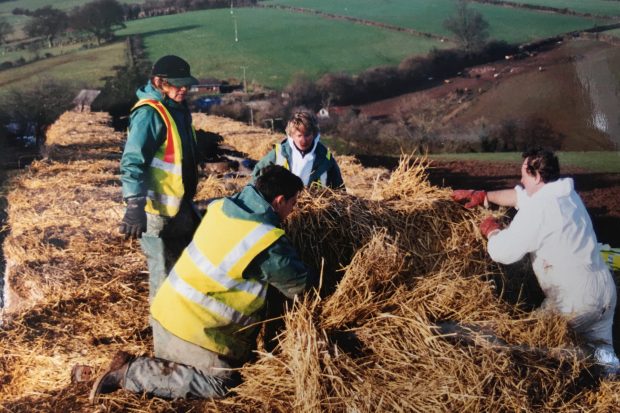 People laying hay bales in a pile